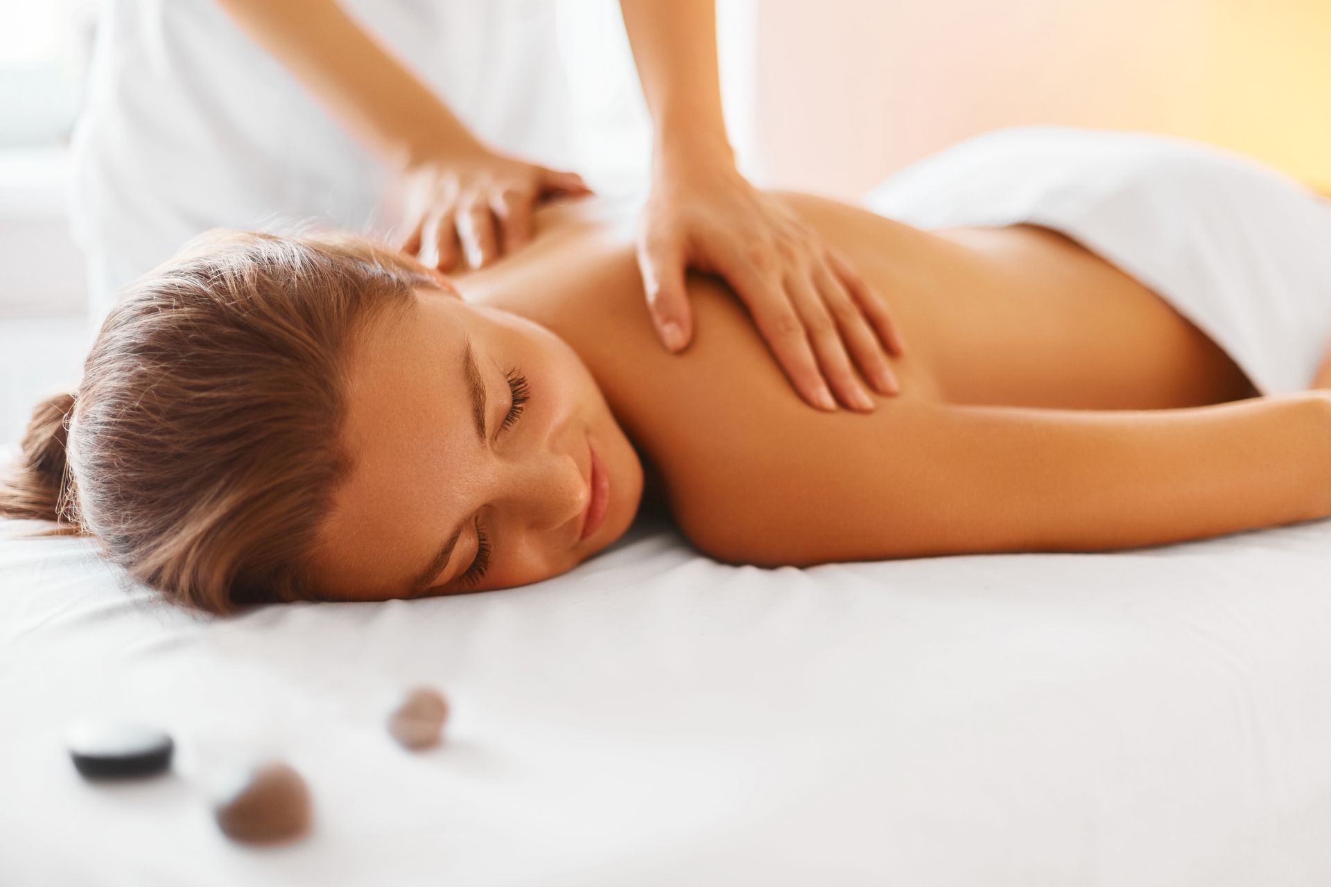 Une personne reçoit un massage du dos sur un lit de spa blanc dans une pièce lumineuse et calme.