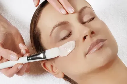 Soin du visage en spa avec application de crème au pinceau sur le visage d'une cliente détendue.
