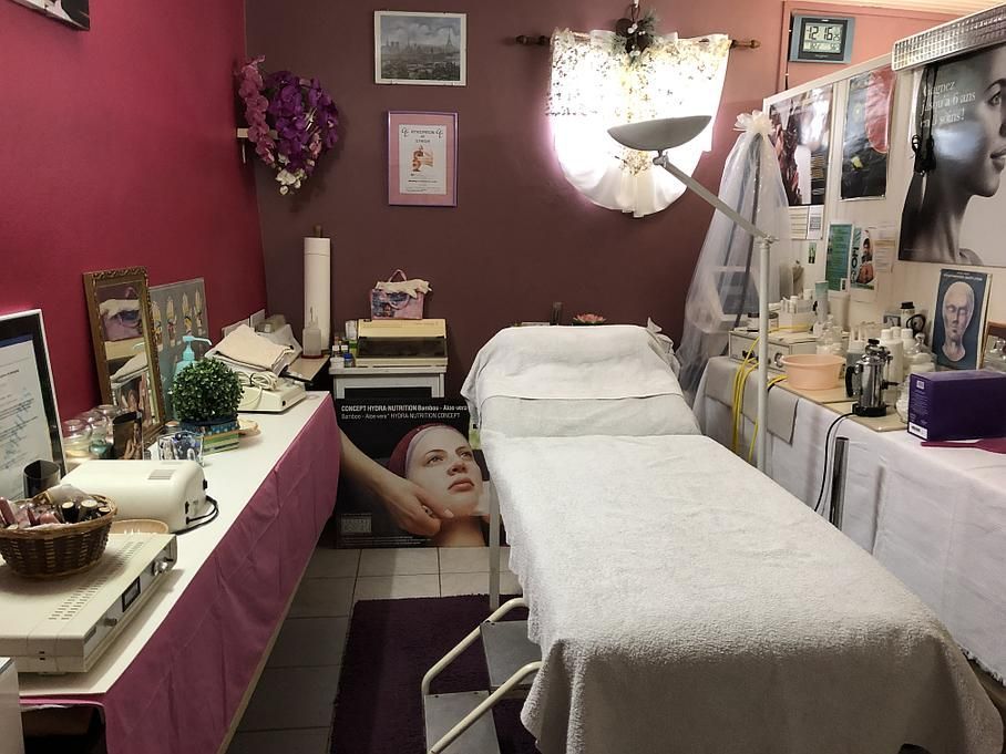 Salle de soins esthétiques avec lit, coiffeuse, étagères et murs roses.