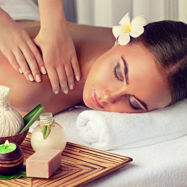 Une femme reçoit un massage de spa sur une serviette blanche, avec des bougies et des produits d'aromathérapie à proximité.
