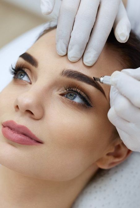 Des mains gantées appliquent un traitement cosmétique sur le front et les sourcils d'une femme lors d'une séance de spa.