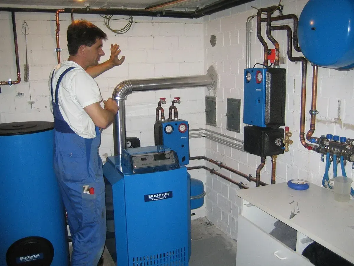 Mann im blauen Overall neben blauem Heizkesselsystem in einem Hauswirtschaftsraum.