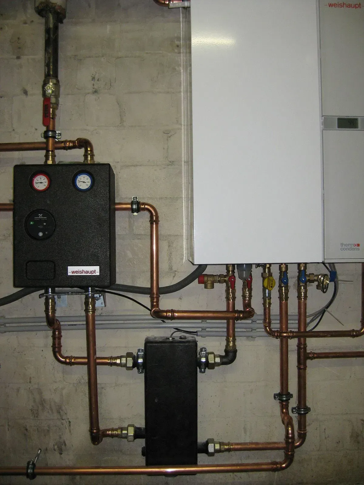 Kupferrohre und Leitungen, die an einen Heizkessel an einer Betonwand angeschlossen sind.