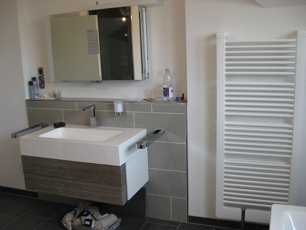 Modernes Badezimmer mit weißem Waschbecken, Spiegel und Handtuchwärmer. Grau geflieste Wand.