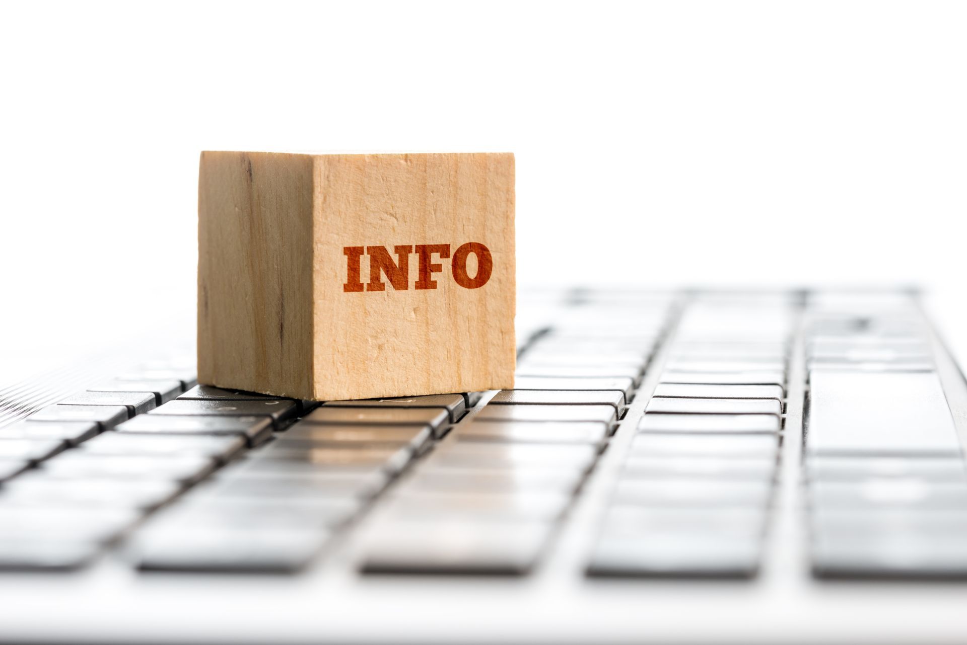 Ein Holzblock mit der Aufschrift „INFO“ liegt auf einer Laptoptastatur.