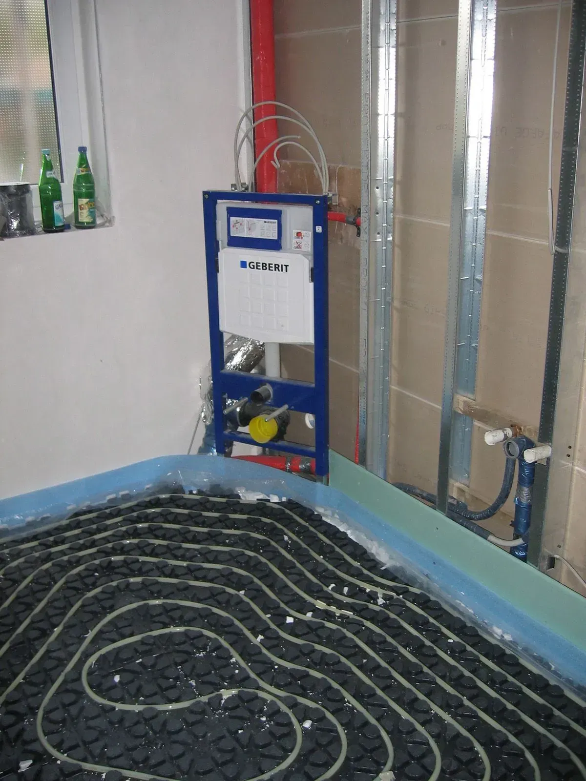 Installation einer Fußbodenheizung, schwarze Rohre auf einem Boden, mit Sanitäranlagen und einem Spülsystem.