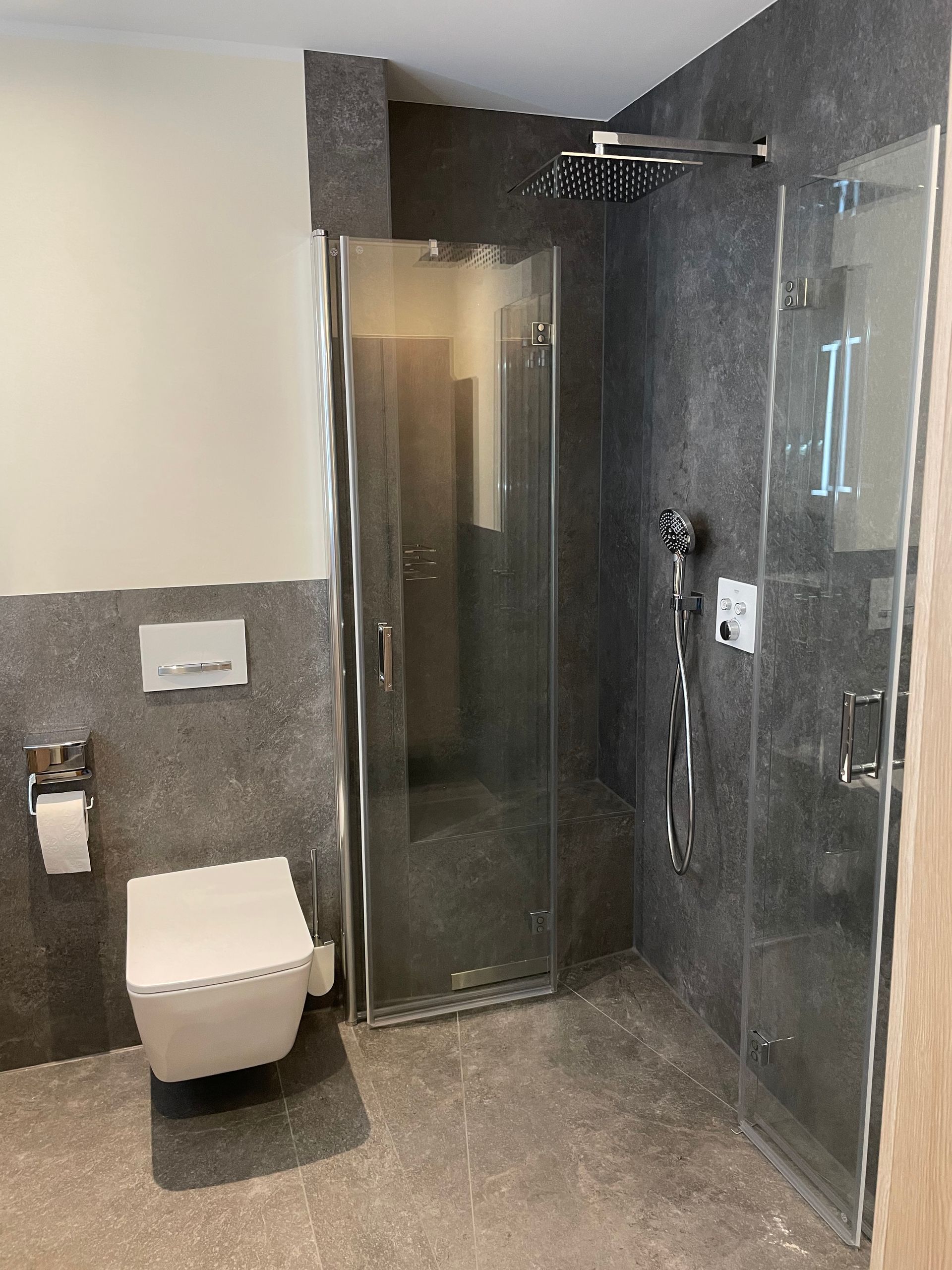 Modernes Badezimmer mit ebenerdiger Dusche, wandhängendem WC und grauen Steinfliesenwänden.