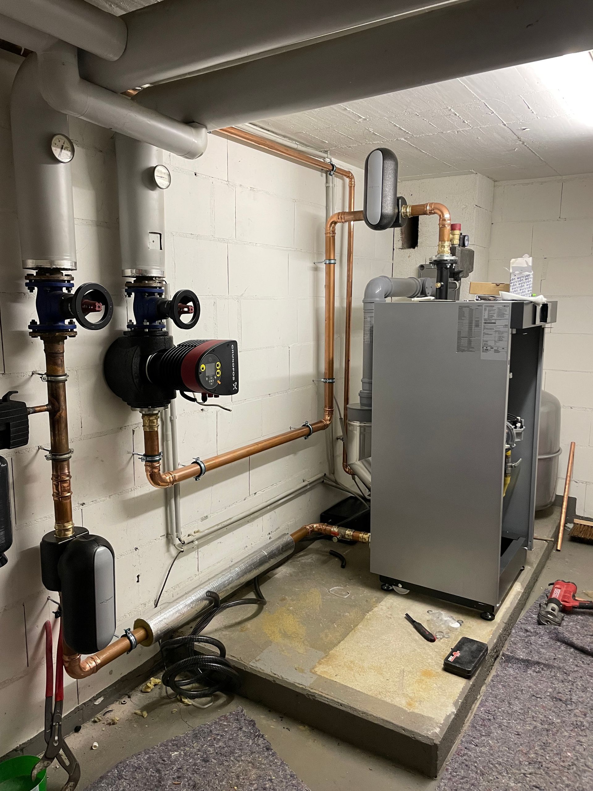 Ein Technikraum mit einem Ofen, Rohren, Pumpen und anderen Geräten vor einer weißen Wand und einem weißen Boden.