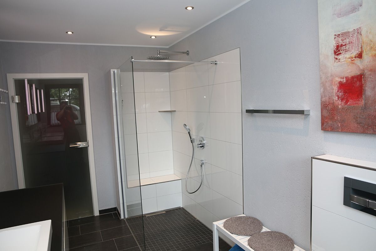 Modernes Badezimmer mit ebenerdiger Dusche. Weiß geflieste Dusche, graue Wände, schwarze Bodenfliesen und Kunstwerke.