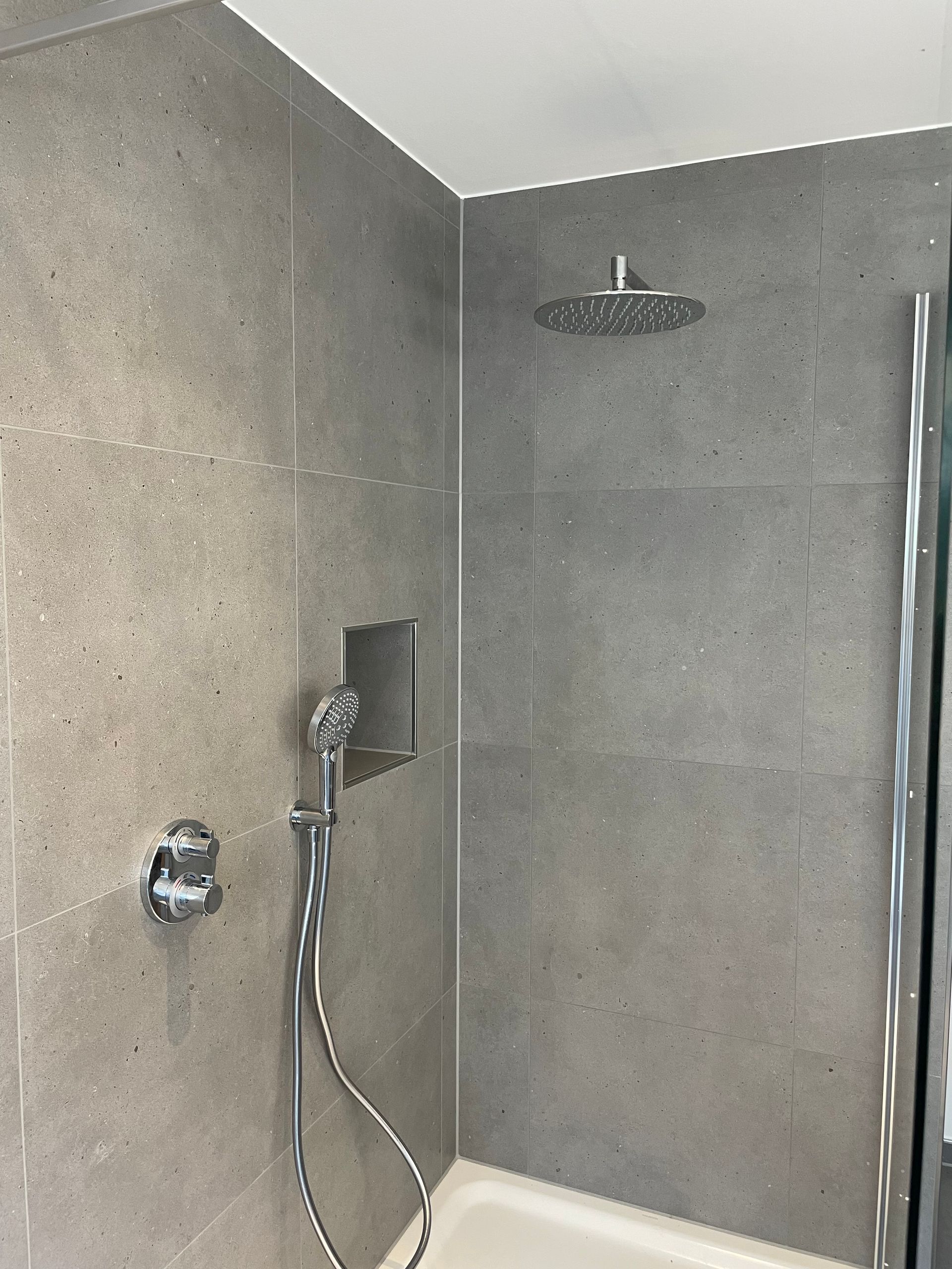 Grau geflieste Dusche mit Regenduschkopf, Handbrause und einer Nische.