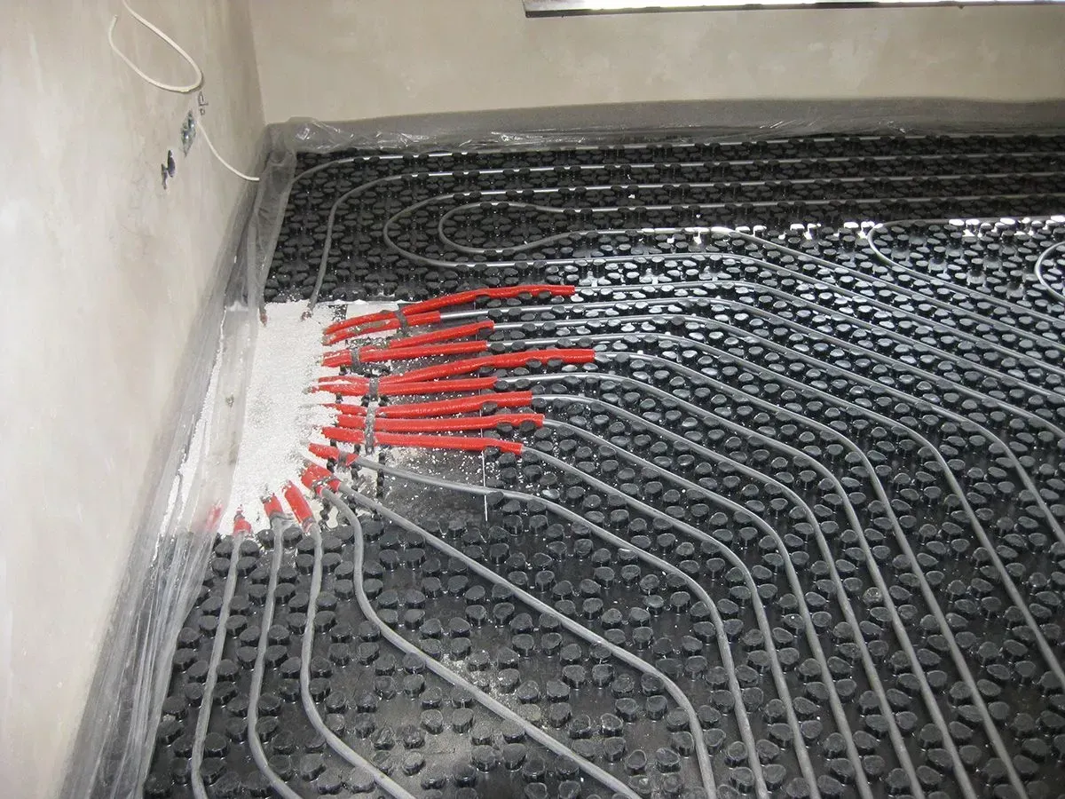 Rohre einer Fußbodenheizung, die auf schwarzen Platten in einem Raum installiert sind. Rote Rohre verbinden.