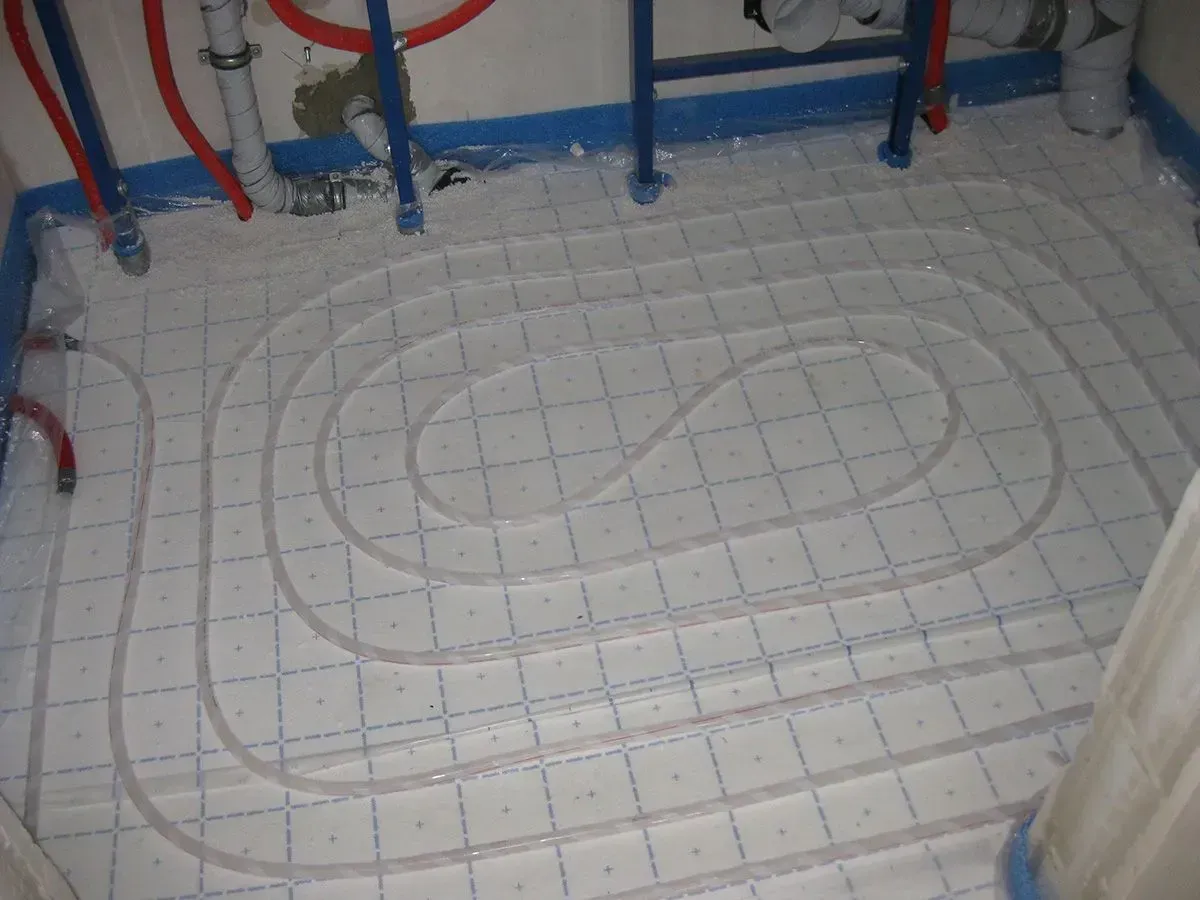 Weiße Rohre schlängeln sich in einem Gittermuster über einen Boden; Teil der Installation einer Fußbodenheizung.