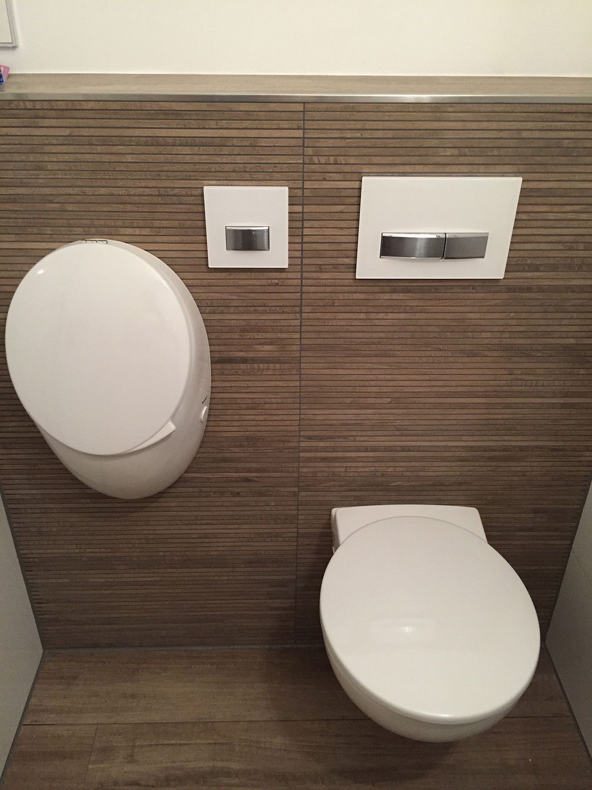 Weißes Wand-WC und Urinal, Spültasten, an brauner strukturierter Wand.