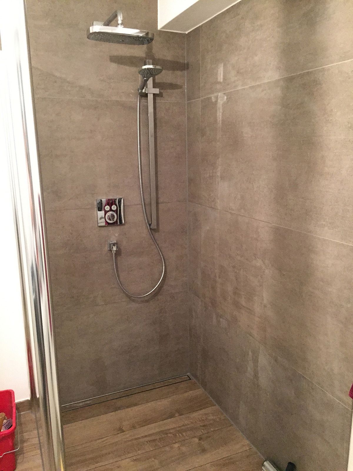 Dusche mit grau gefliesten Wänden, Regenduschkopf und Holzboden.