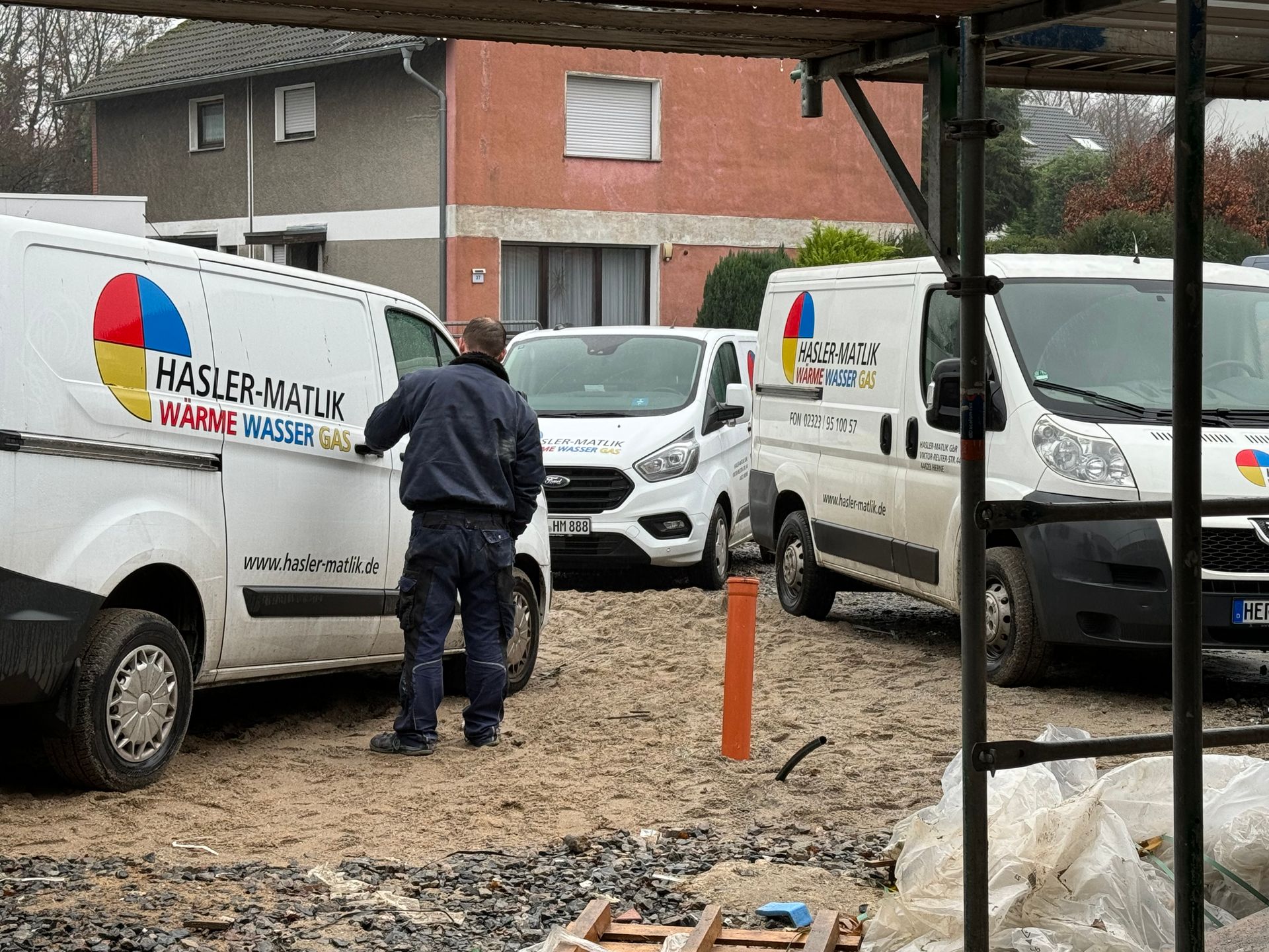 Drei Servicefahrzeuge parken in der Nähe eines Hauses, in dem ein Bauarbeiter arbeitet.