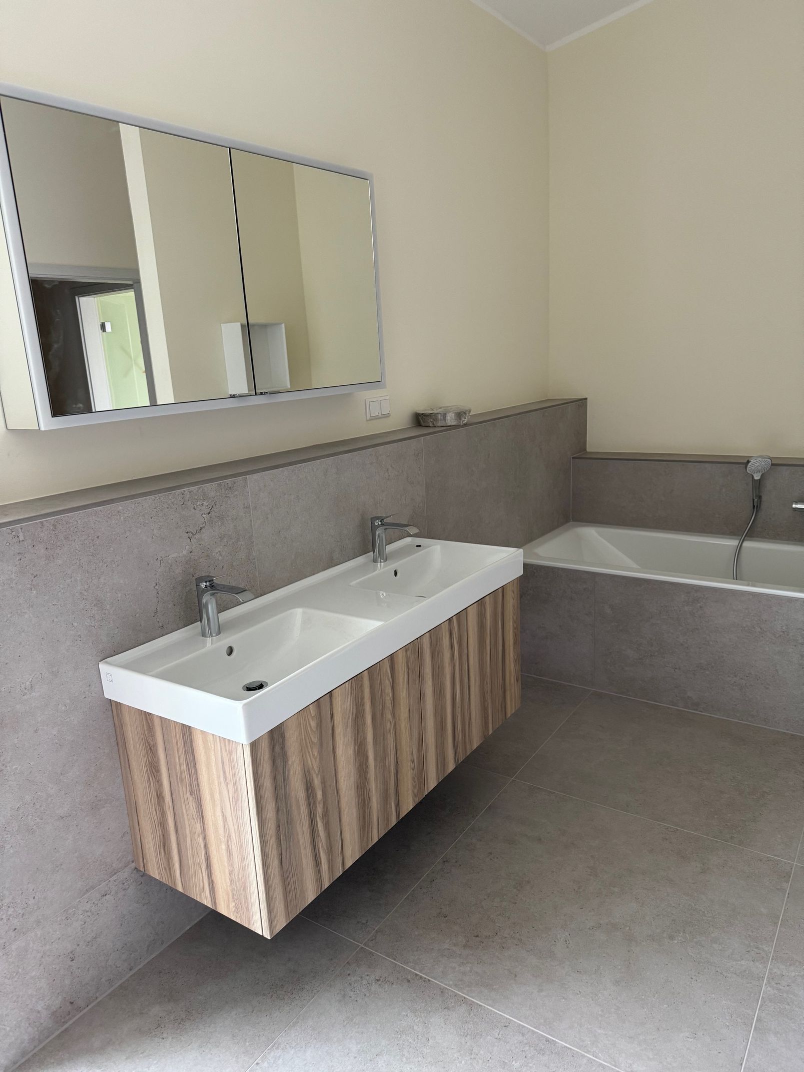 Badezimmer mit Doppelwaschbecken, Holzschrank, Betonwänden und großem Spiegel.