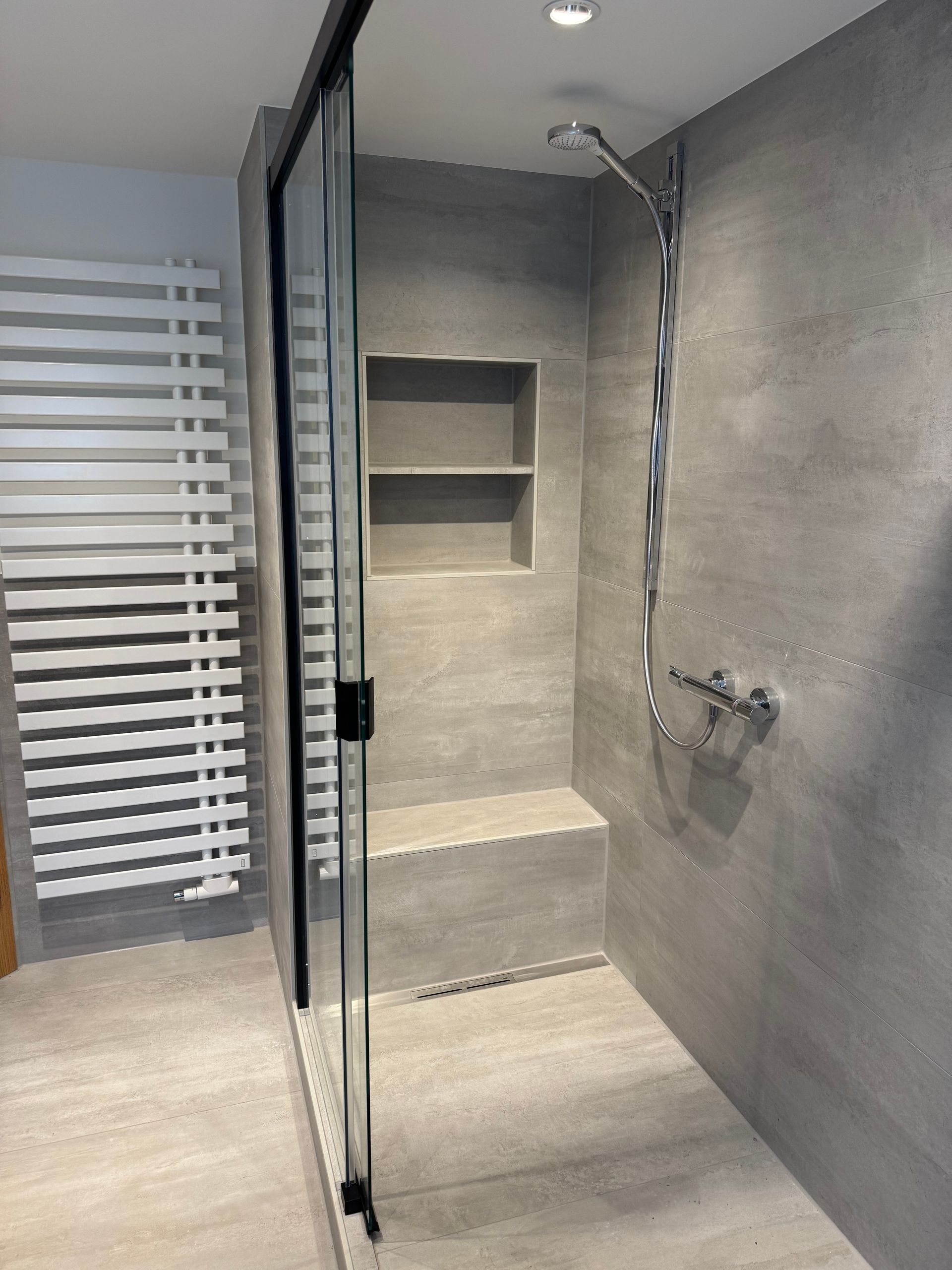 Modernes Badezimmer mit grau gefliester Dusche und Glastür, eingebauten Regalen und Chromarmaturen.