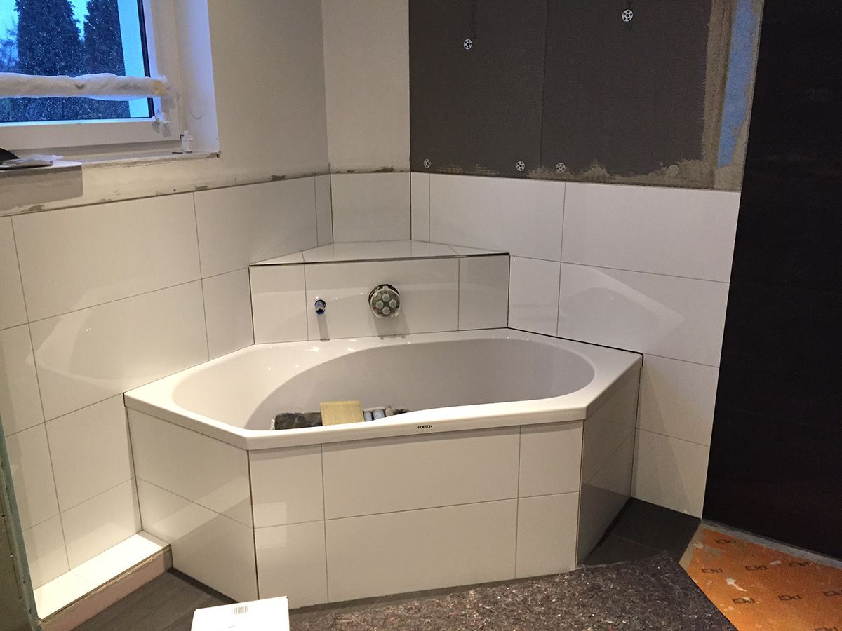 Badezimmer mit weißer sechseckiger Badewanne, weiß gefliesten Wänden und Fenster.