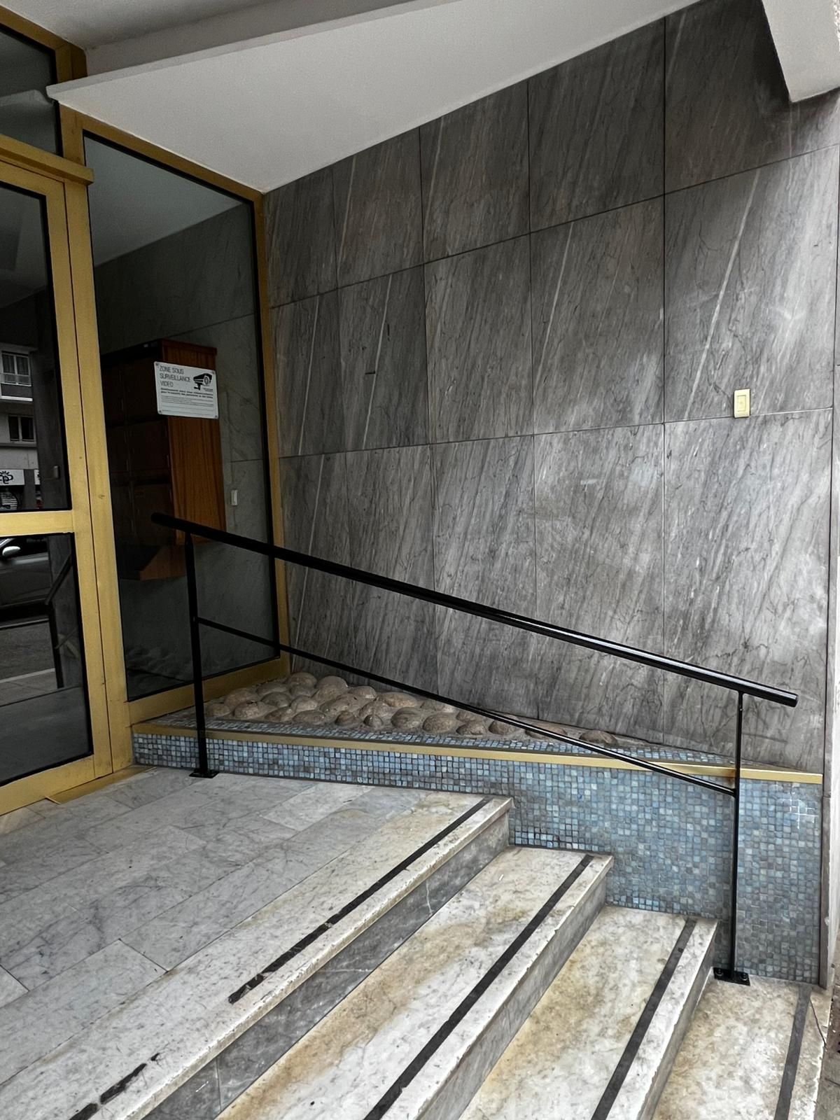 Escalier en pierre avec rampe noire et murs carrelés gris à l'intérieur d'un bâtiment