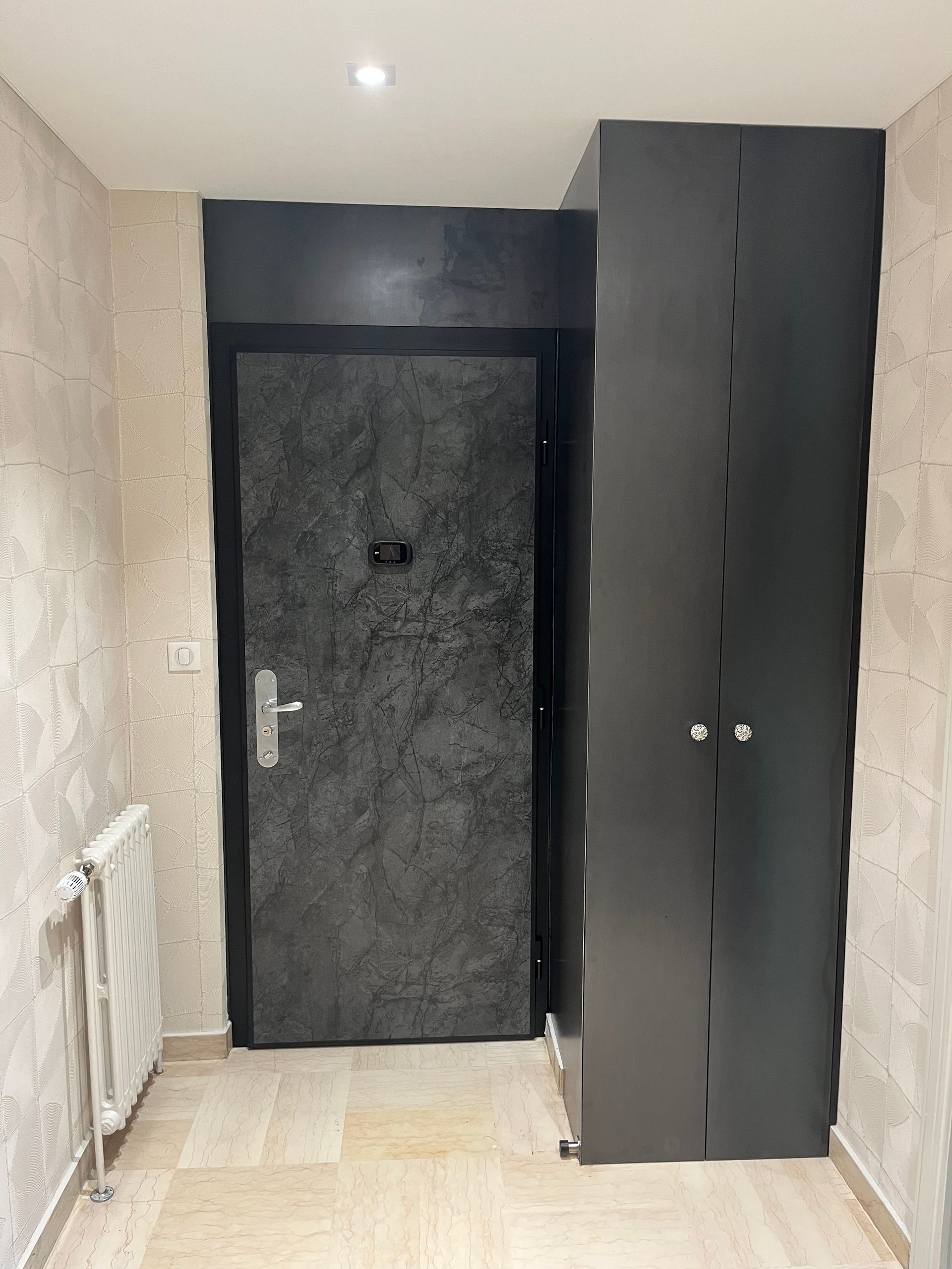 Couloir étroit avec une porte noire au fond et une grande armoire sombre sur la droite.