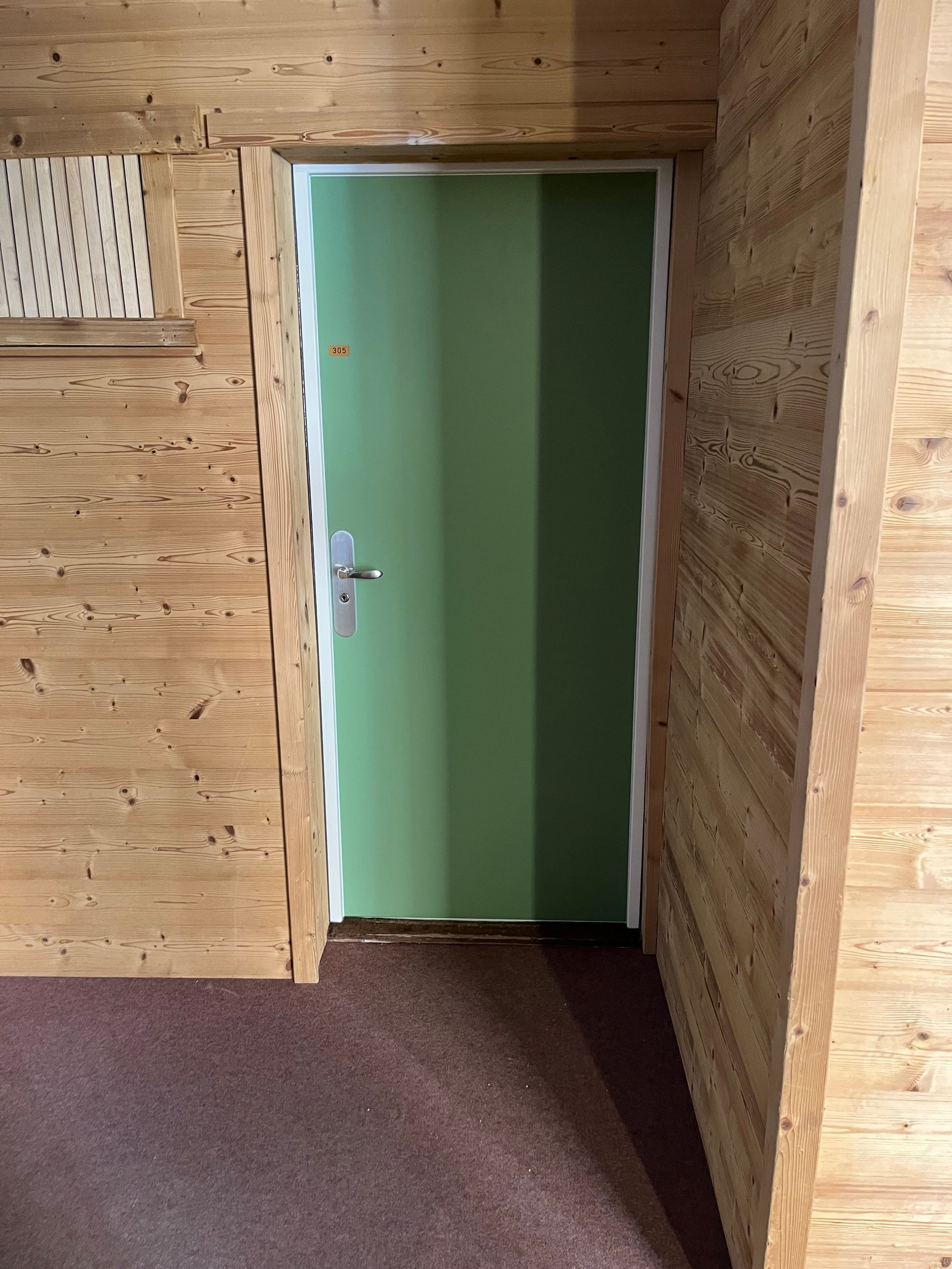 Porte verte encastrée dans un mur lambrissé.