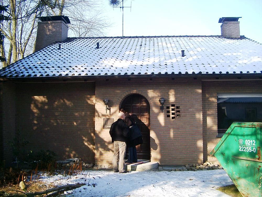 Ein grüner Müllcontainer steht vor einem Backsteinhaus