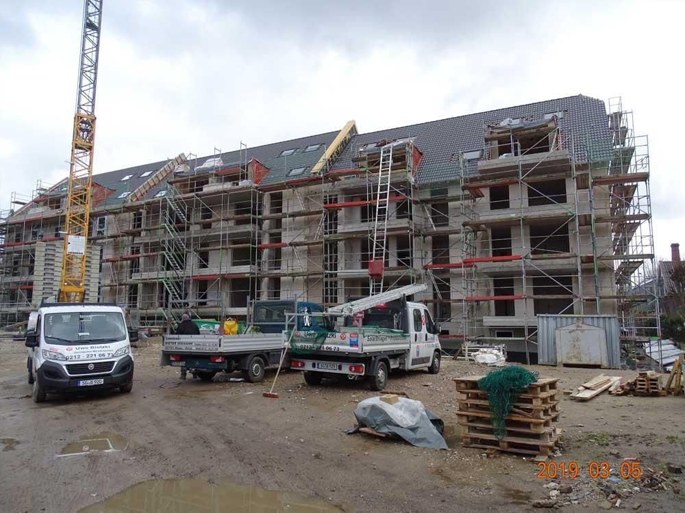 Ein im Bau befindliches Gebäude mit Gerüsten und davor geparkten Lastwagen