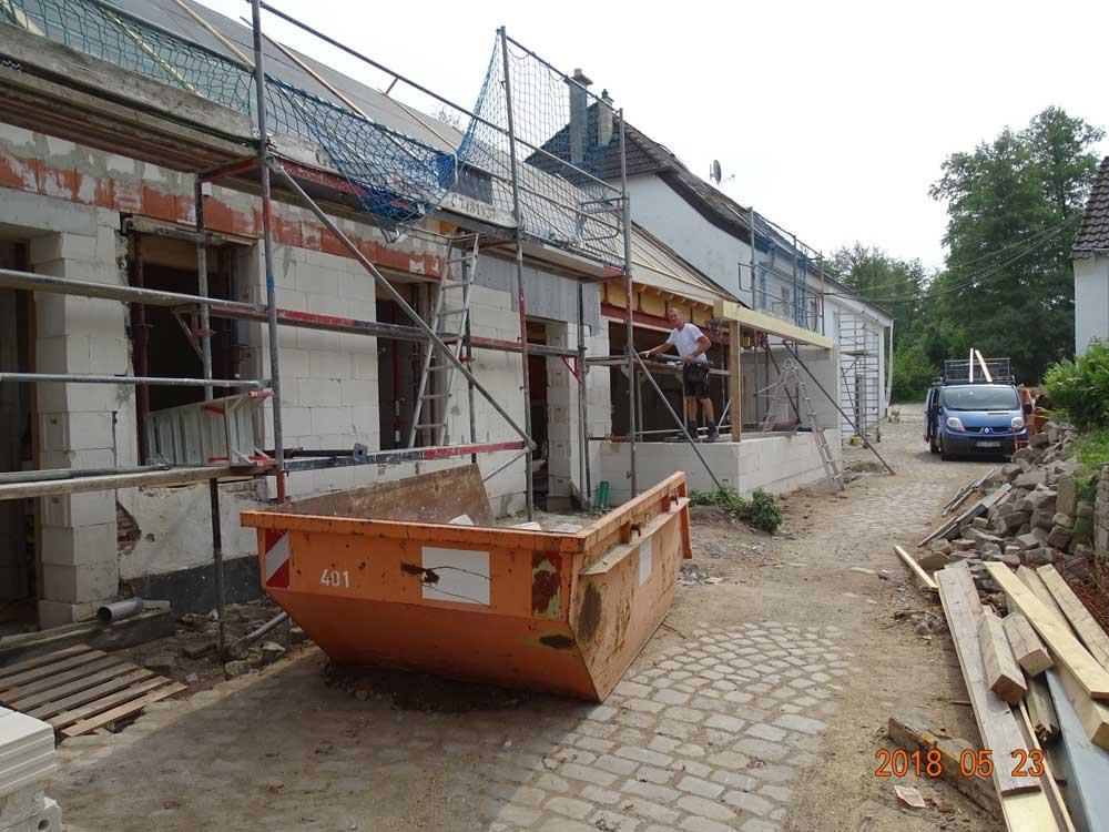 Ein großer orangefarbener Müllcontainer steht vor einem im Bau befindlichen Gebäude