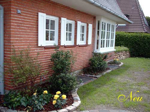 Ein Backsteinhaus mit weißen Fensterläden und Blumen davor