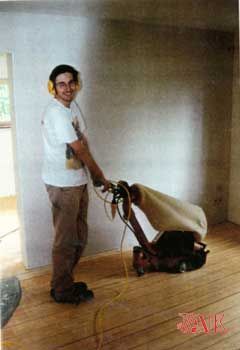 Ein Mann schleift mit einer Maschine einen Holzboden.