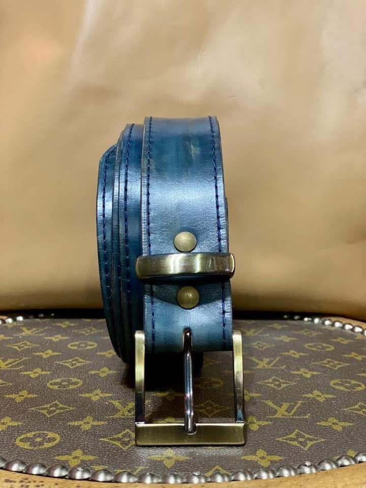Cinturón de cuero azul con una hebilla plateada sobre una superficie estampada, sobre un fondo tostado