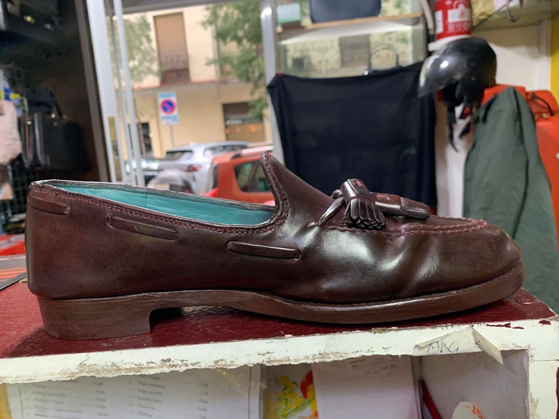 Mocasín de cuero marrón sobre una estantería blanca, con plantilla verde azulado, en una tienda