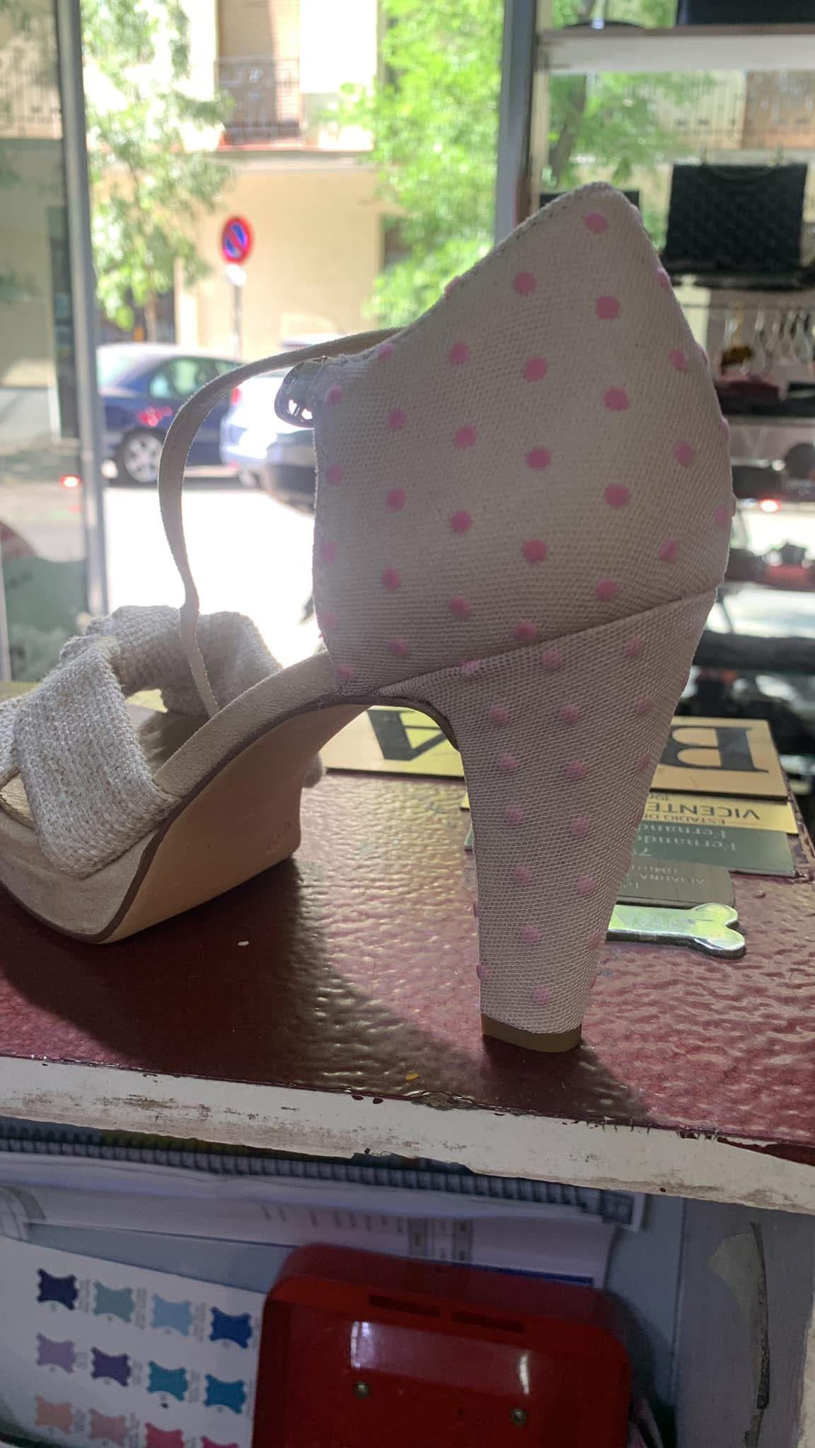 Zapatos de tacón alto rosas con lunares, expuestos sobre un mostrador junto al escaparate de una tienda