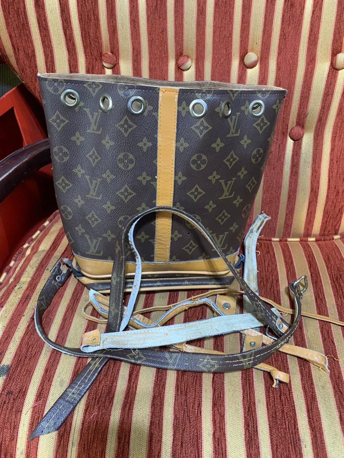 Bolso de Louis Vuitton con monograma, correas y asas, colocado sobre una silla de rayas rojas