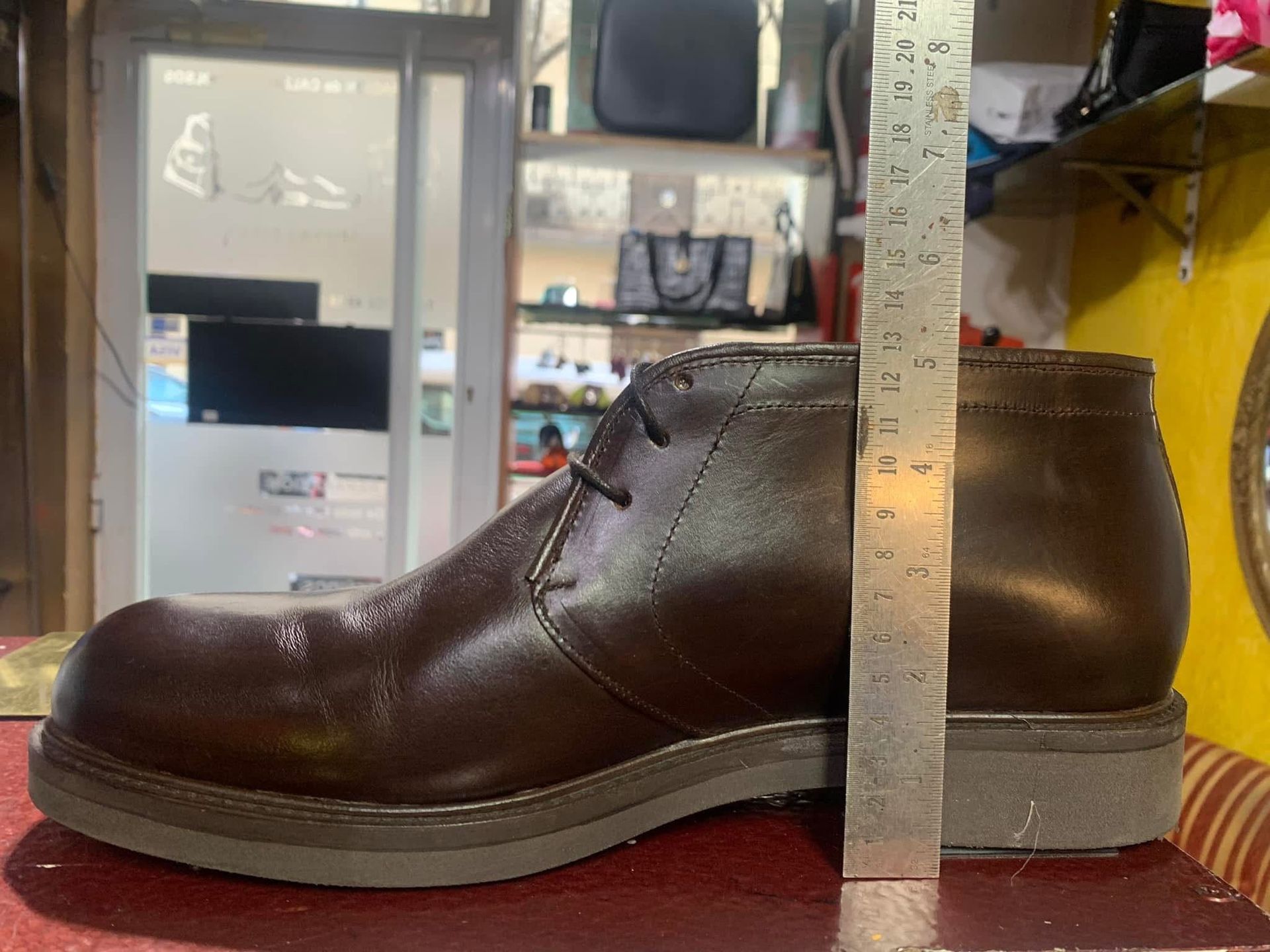 Bota de cuero marrón junto a una regla de medir sobre una superficie roja en una zapatería