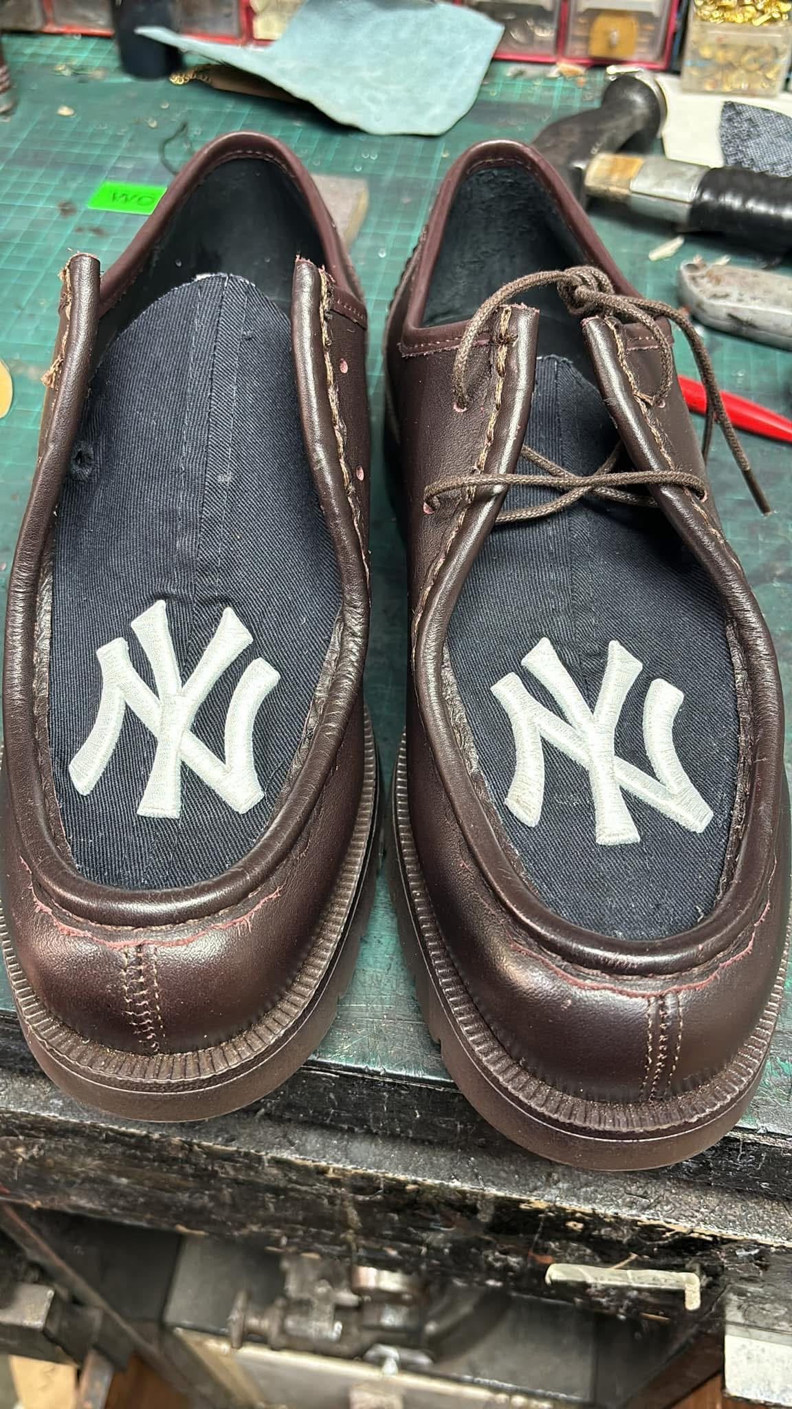 Par de zapatos sin cordones de cuero marrón de los New York Yankees con logotipos blancos sobre un banco de trabajo