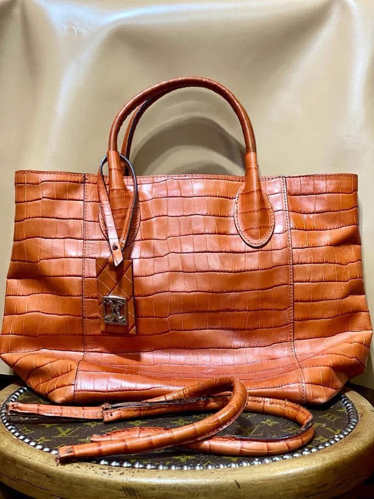 Bolso tote de piel naranja con textura de piel de cocodrilo, asas dobles y correa para el hombro sobre un fondo neutro