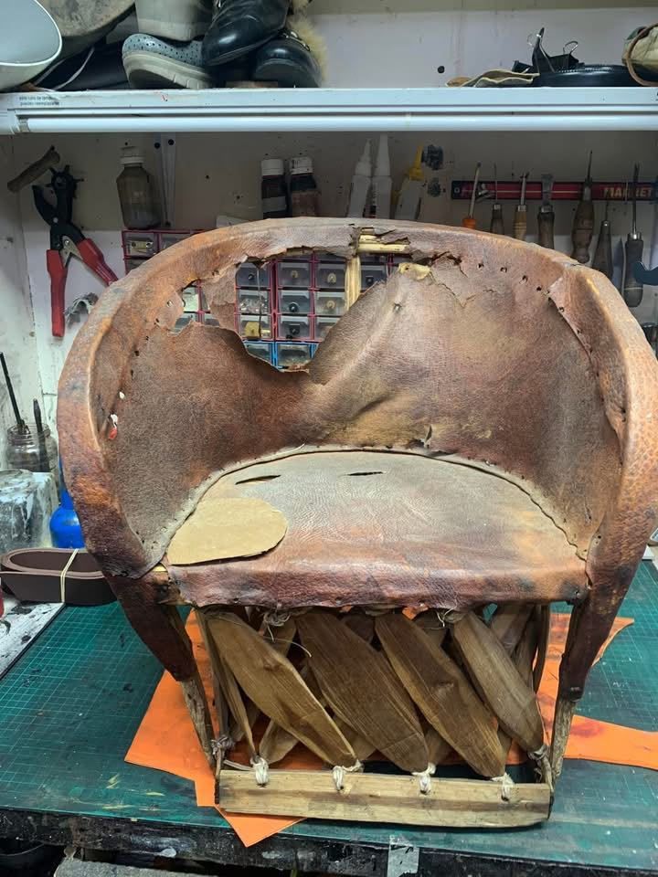Sillón de cuero marrón desgastado en un taller, con el tapizado rasgado y la estructura de madera expuesta.