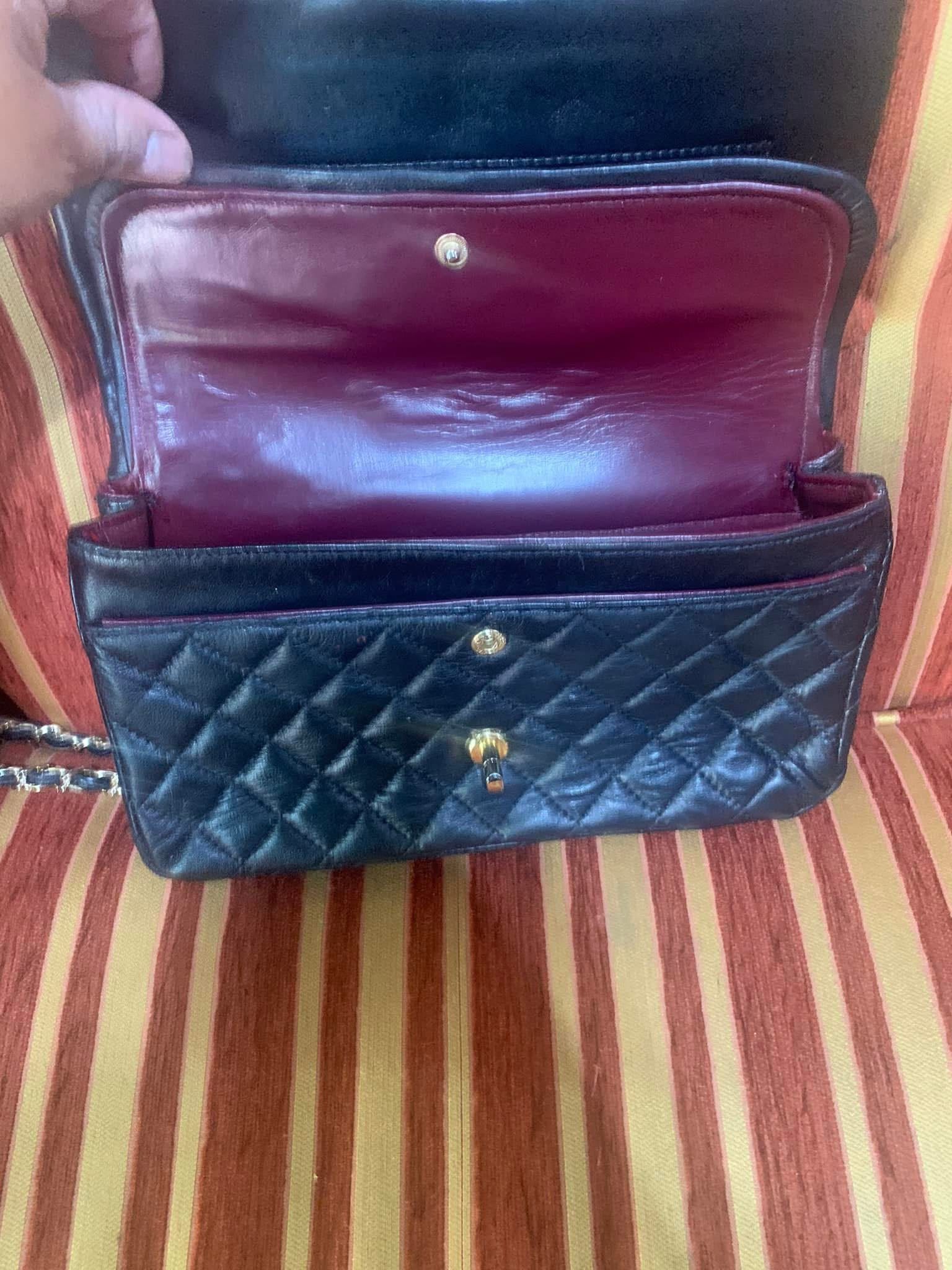 Cartera negra acolchada con el interior burdeos, abierta sobre una superficie de tela a rayas.
