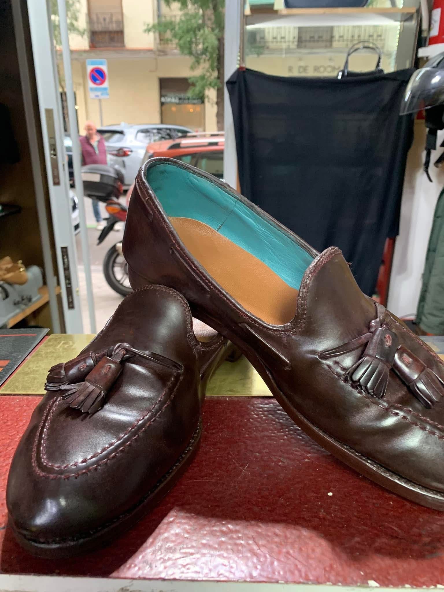 Dos mocasines de cuero marrón, uno abierto para mostrar una plantilla turquesa, sobre el mostrador de una tienda.
