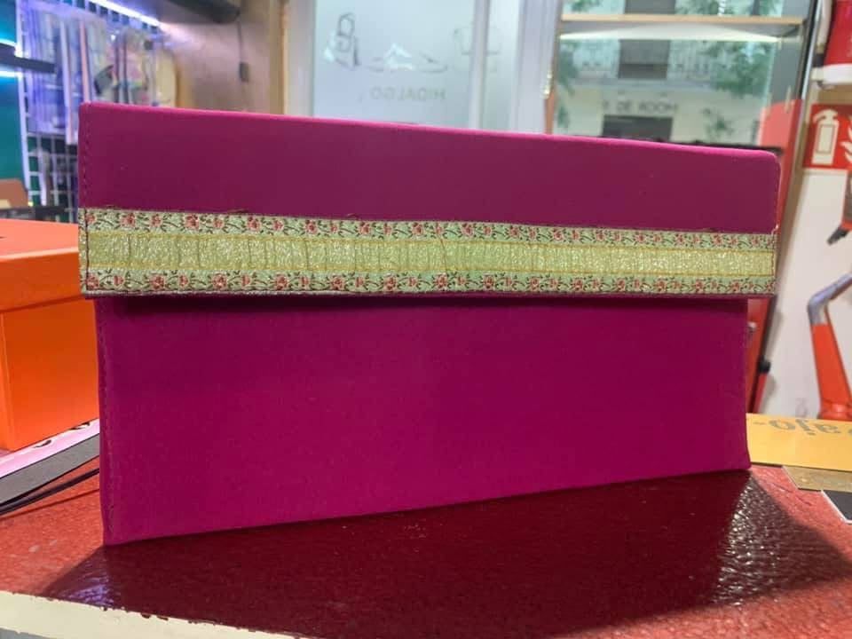 Caja de regalo magenta con un lazo dorado con purpurina sobre una mesa oscura, en una zona de exposición de una tienda