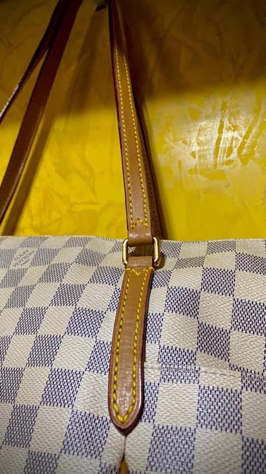 Correa marrón de cuero con una hebilla sobre un bolso de cuadros amarillos y azules