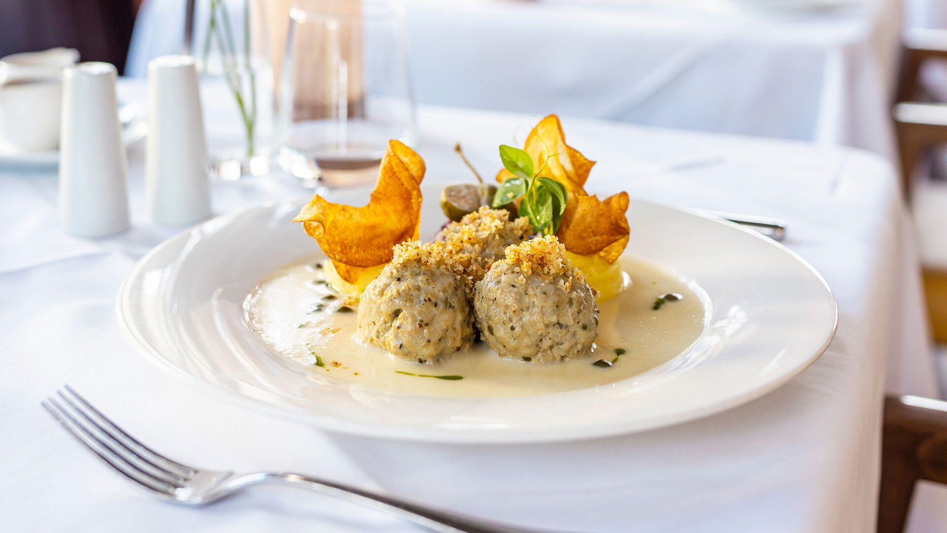 Ein Teller mit Essen: Teigtaschen, gebratene Kartoffelbeilage, Soße, auf einer weißen Tischdecke.
