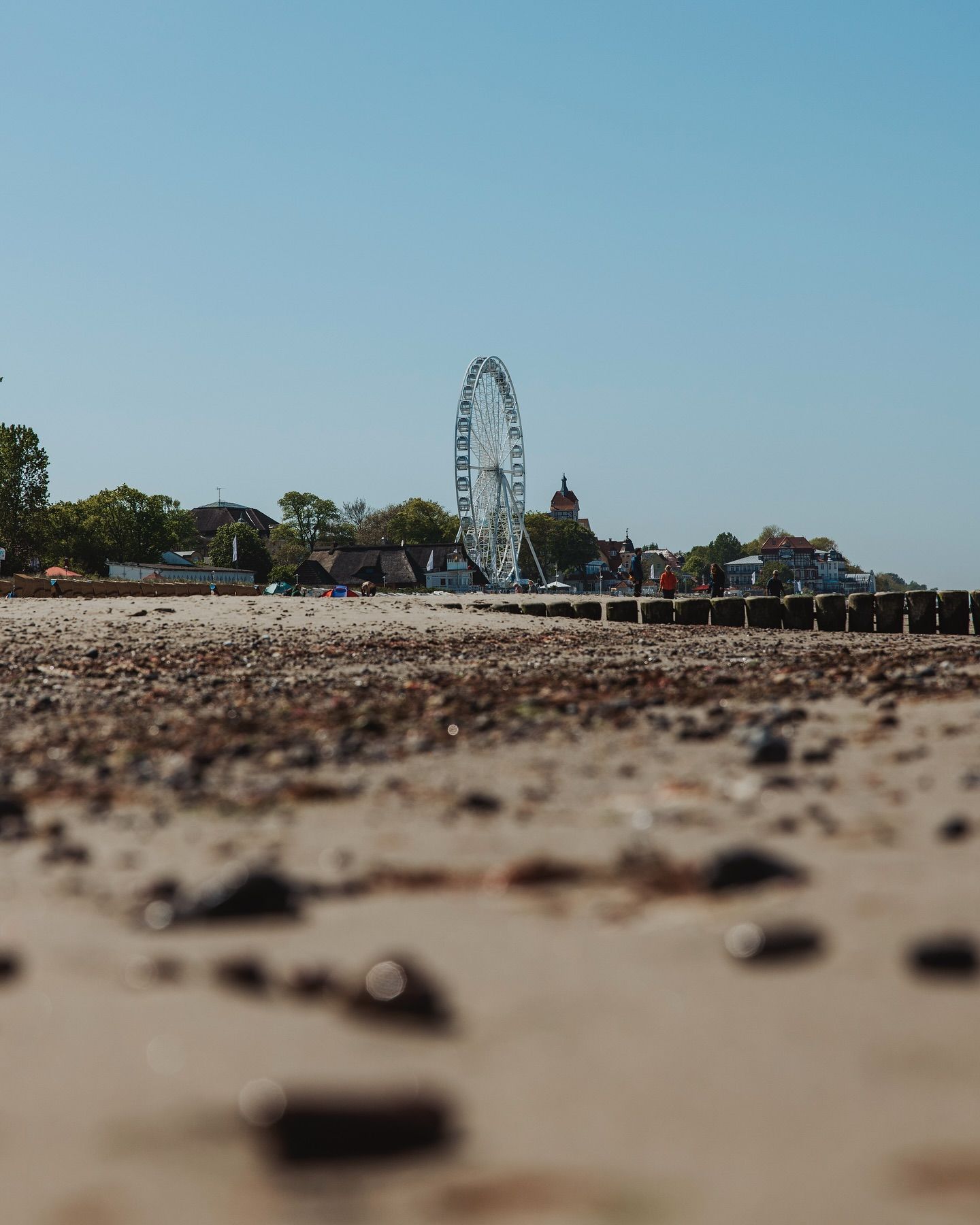 In der Ferne steht ein Riesenrad an einem Sandstrand unter einem klaren, strahlend blauen Himmel.
