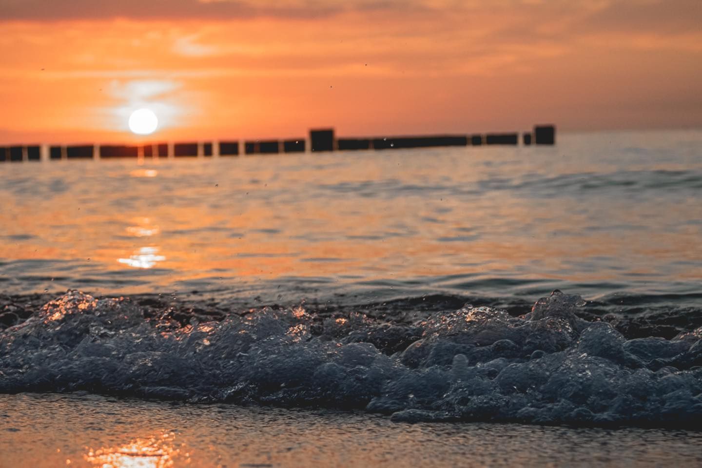 Ein goldener Sonnenuntergang taucht die sanft an einen sandigen Strand plätschernden Wellen in ein warmes Licht.