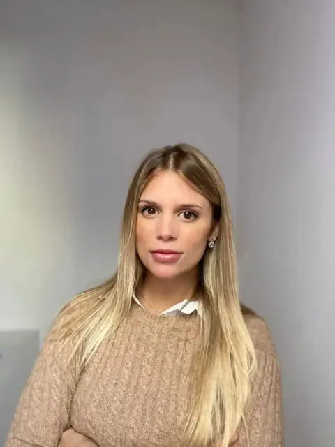 Mujer rubia de pelo largo, vestida con un suéter marrón