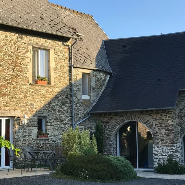 Une ferme en pierre au toit d'ardoise possède une entrée voûtée au rez-de-chaussée et un petit patio.