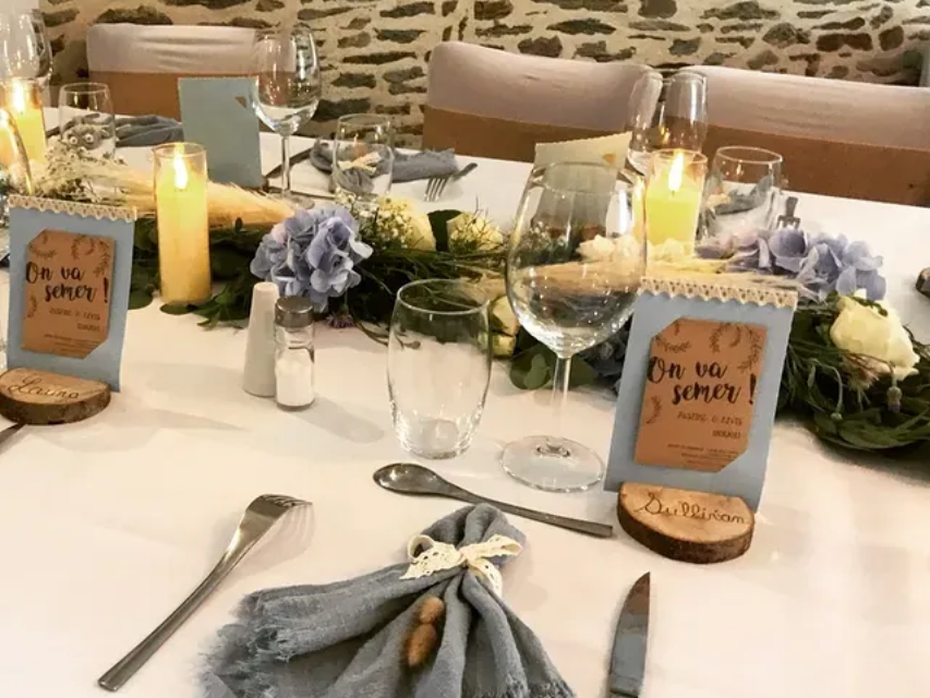 Une table de mariage rustique dressée avec des serviettes bleues, des bougies, des fleurs et des marques places manuscrits.