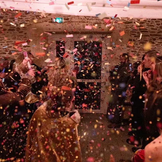 Un groupe de personnes en tenue de fête célèbre à l'intérieur tandis qu'une pluie de confettis colorés tombe autour d'elles.