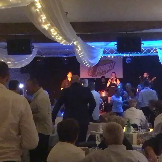 Un groupe de musique joue en direct sur une scène décorée de lumières et de tissus lors d'un événement en intérieur faiblement éclairé, les invités étant assis à proximité.